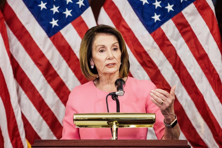 Pelosi speaking at a podium with an American flag behind her.